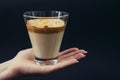 Glass of trendy Korean coffee in the palm of hand on a black background