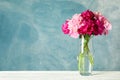 Glass vase with bouquet of beautiful peonies on white table against blue background Royalty Free Stock Photo