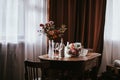 Glass vase with flowers on a wooden table in front of a light background. On the table are a bottle and glass wine glasses. Royalty Free Stock Photo