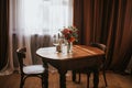 Glass vase with flowers on a wooden table in front of a light background. On the table are a bottle and glass wine glasses. Royalty Free Stock Photo