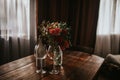 Glass vase with flowers on a wooden table in front of a light background. On the table are a bottle and glass wine glasses. Royalty Free Stock Photo