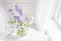Glass vase with lilac and white floweers  in light cozy bedroom interior. White wall, sunlight from window, copy space Royalty Free Stock Photo