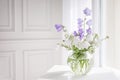 Glass vase with lilac and white floweers  in light cozy bedroom interior. White wall, sunlight from window, copy space Royalty Free Stock Photo