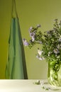 Vertical image.Glass vase and New York asters on the table and blue apron on the wall