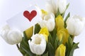 A glass vase with white and yellow tulips and a little heart card