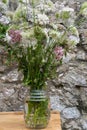 Glass vase with wild flowers on rustic wooden table, gray stone wall background, in Cantabria, Royalty Free Stock Photo