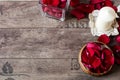 Glass vase and wood bow filled with red and white rose petals, white aromatic vanilla candle. Wooden background. Aromatherapy