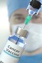 Glass vial with cancer vaccine and syringe against blurred doctor`s face. 3D rendering