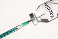 Glass vial with label Vaccine on white background, green hypodermic syringe needle inside - vaccination concept Royalty Free Stock Photo