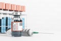 Glass vial with vaccine against coronavirus and syringe with test-tubes with red caps in background. Mock up Royalty Free Stock Photo