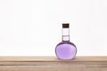 Glass vintage bottle with a brown cork and purple liquid on a wooden table with white background. Royalty Free Stock Photo