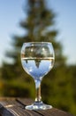 A glass with a water on the balcony overlooking the mountains. Mirror display in a glass. Display a conifer tree in a glass