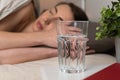 A glass of water by bed with a beautiful young woman in background sleeping