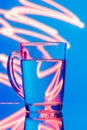 Glass of water on a blue background with a yellow abstraction, glare of light