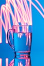 Glass of water on a blue background with a yellow abstraction, glare of light