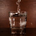 A clear stream of water pours into a glass on a braun background