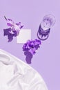 Glass with water and card note with iris flower on pastel violet background with white silk cloth. Summer refreshment concept. Royalty Free Stock Photo