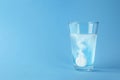 Glass of water with effervescent tablet on blue background, space for text