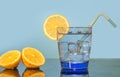 A glass of water, ice, lemon, and straw sits on a table with a blue background. Preparing a fresh drink with lemon juice. Sliced Royalty Free Stock Photo