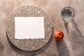 Glass of water and red apple in sunlight with long shadows on a beige grunge background. Blank card on a granite plate, invitation