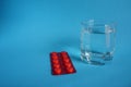 Glass of water with red plate of pills on blue background Royalty Free Stock Photo