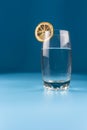 Glass of water with a slice of dried lemon on a blue background