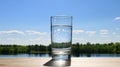 Glass of water on table in front of green landscape. Fresh mineral healthy drinking water. Transparent aqua summer sky