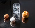 Glass of water with two eggs placed beside it on a dark background.