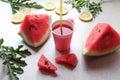 A glass of watermelon juice with a drinking straw on a background of watermelon slices and lemon slices on a gray background, side