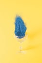 A glass from which scattered blue sequins fall outon a yellow background. Party celebration drink concept Royalty Free Stock Photo