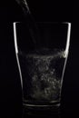 glass glass in which water flows on a black background. The water is clean - the glass is transparent. A glass on a black backgrou Royalty Free Stock Photo