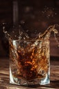 Glass glass with whiskey or cognac, frozen drink splashes from a thrown ice cube, table top made of natural aged wood, concept for Royalty Free Stock Photo