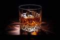 Glass of whiskey with cube of ice on wooden table with black background