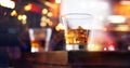 Glass of whiskey drink with ice cube on wooden table