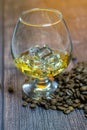 A glass of whiskey with ice and coffee beans on a wooden table. Strong alcohol with ice. Vintage close-up of golden cognac.