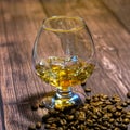 A glass of whiskey with ice and coffee beans on a wooden table. Strong alcohol with ice. Vintage close-up of golden cognac.