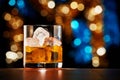 Glass of whiskey with ice on colorful Christmas lights background