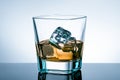 Glass of whiskey with ice cubes on bar table with reflection on light blue tint background Royalty Free Stock Photo