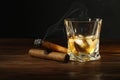 Glass of whiskey with ice cubes and cigars on wooden table