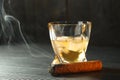 Glass of whiskey with ice cubes and smoldering cigar on black wooden table, closeup. Space for text Royalty Free Stock Photo