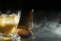 Glass of whiskey with ice cubes and smoldering cigar on black wooden table, closeup. Space for text Royalty Free Stock Photo