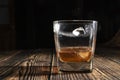 Glass of whiskey with ice cubes on a wooden table. An old tabletop with light and a glass of strong drink. Royalty Free Stock Photo