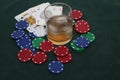 A glass of whiskey with ice on the rocks with poker chips and a hand of cards on green braise background