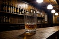 glass of whiskey on the rocks on wooden pub counter with liquors on the shelf in background