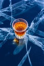 A glass of whiskey stands on beautiful ice with deep cracks.