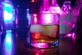 Glass of whisky on wooden bar closeup with bottles blurred view on dark background with light and smoke. Single glass of whisky on Royalty Free Stock Photo