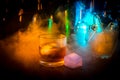 Glass of whisky on wooden bar closeup with bottles blurred view on dark background with light and smoke. Single glass of whisky on Royalty Free Stock Photo