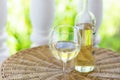 Glass of white dry wine and bottle on wicker table on garden terrace of villa or mansion. Authentic lifestyle image. Royalty Free Stock Photo