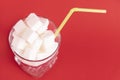 A glass of white glass with a straw filled with white cubes of refined sugar on a red background. Copy space Royalty Free Stock Photo