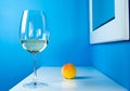 A glass of white wine on a blue background is standing on a white table with a peach